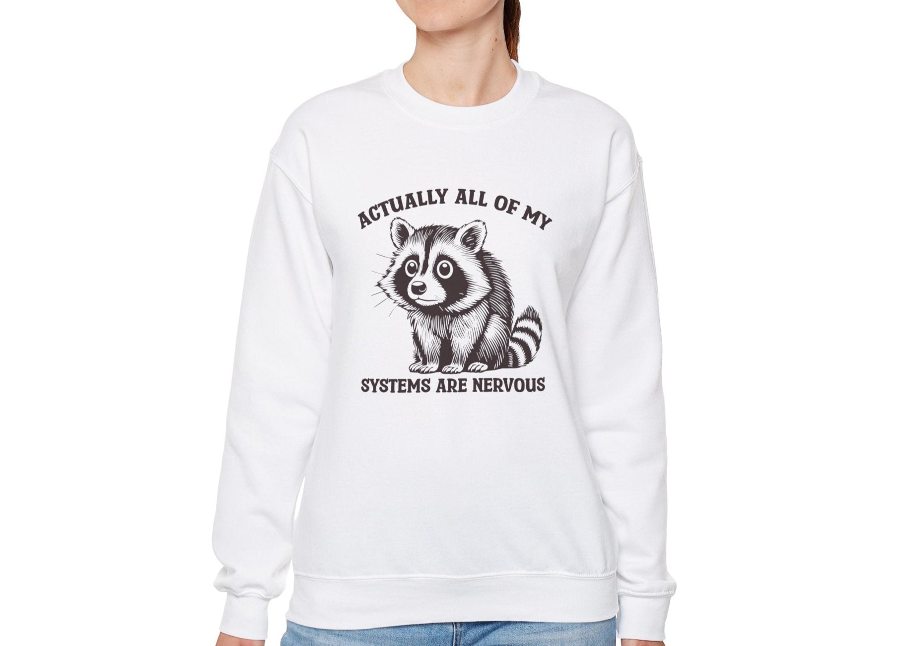 Model wearing a white sweatshirt with a raccoon graphic and the text "Actually All of My Systems Are Nervous," standing with hands at sides. Part of the Vivid Divergence Sensory Friendly Unisex Sweater Jumper Range.