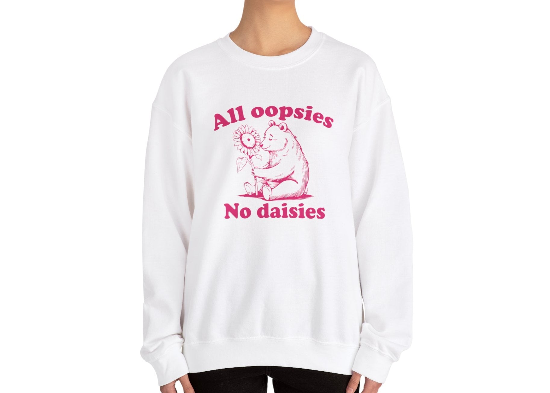 Model wearing a white sweatshirt with a cartoon bear holding a sunflower and the text "All Oopsies, No Daisies," standing with hands at sides. Part of the Vivid Divergence Sensory Friendly Unisex Sweater Jumper Range.