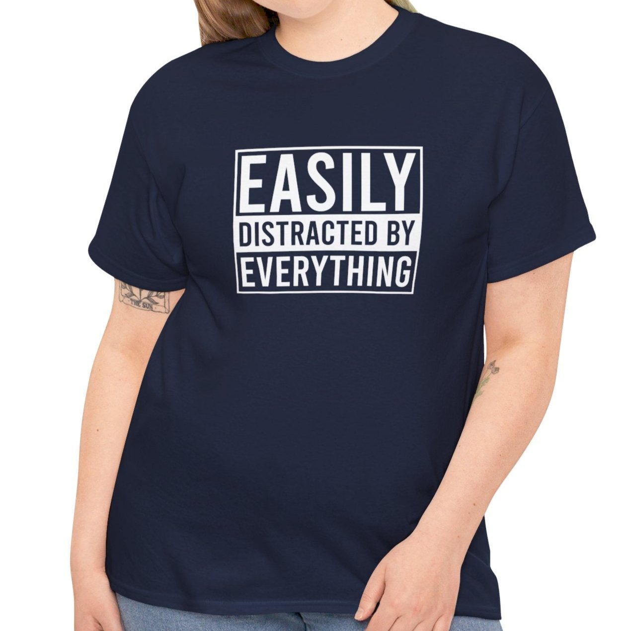 A person wearing a navy blue T-shirt with "Easily Distracted by Everything" text, shown in a casual pose. Part of the Vivid Divergence Sensory Friendly Unisex Tees Range.