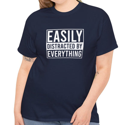 A person wearing a navy blue T-shirt with "Easily Distracted by Everything" text, shown in a casual pose. Part of the Vivid Divergence Sensory Friendly Unisex Tees Range.