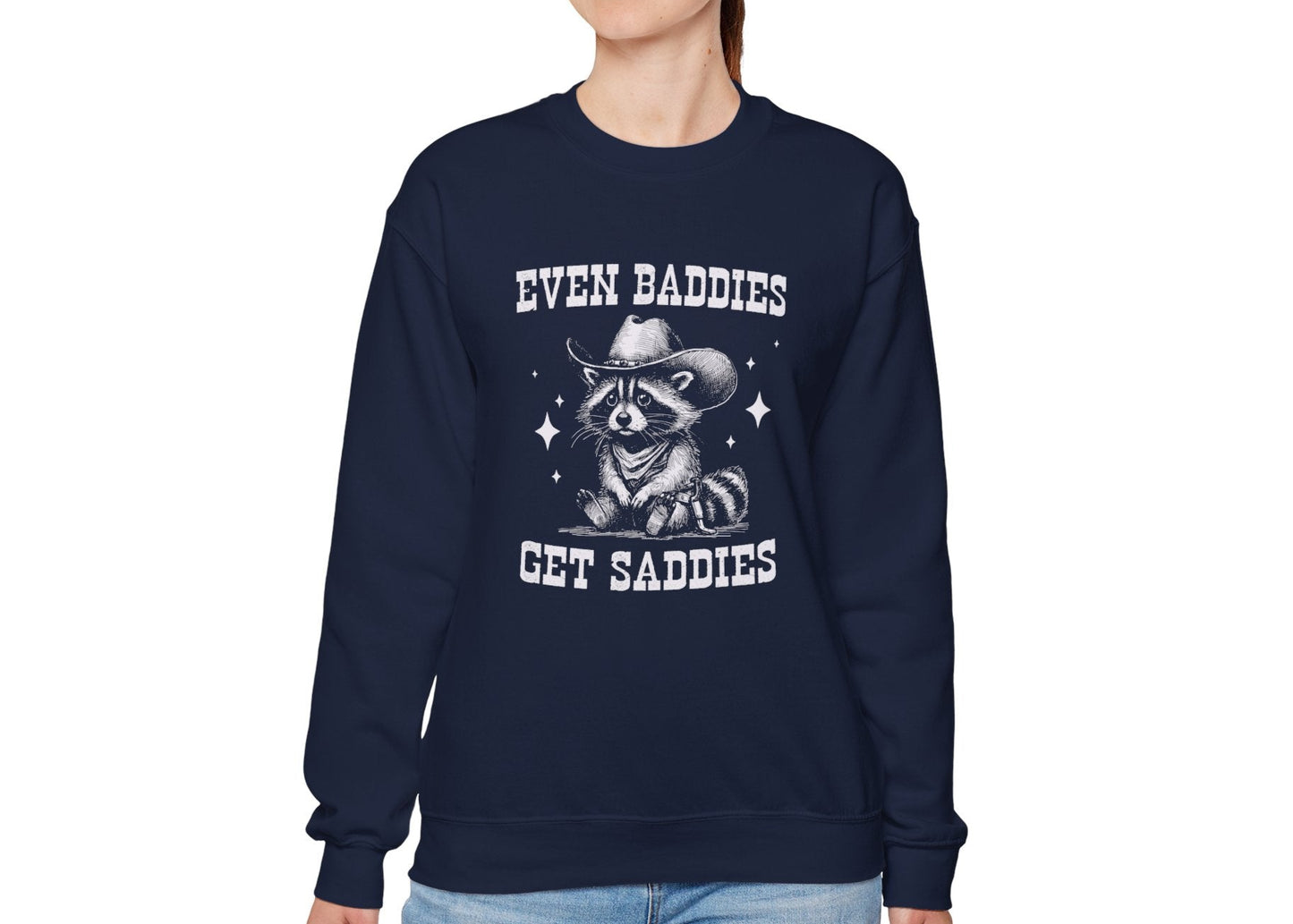 Model wearing a navy blue sweater jumper with the text "Even Baddies Get Saddies" and a cartoon raccoon illustration. Part of the Vivid Divergence Sensory Friendly Unisex Sweater Jumper Range.