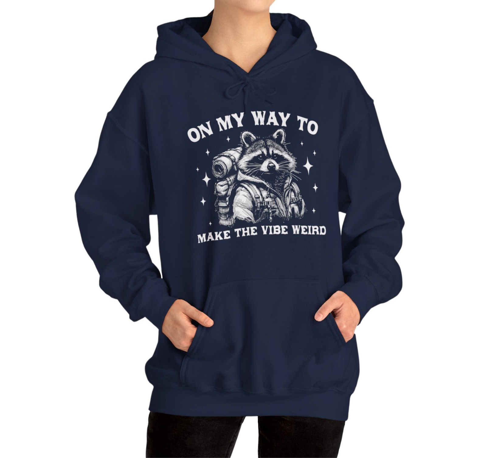 Model wearing a navy blue hoodie featuring the text "On My Way to Make the Vibe Weird" and a cartoon illustration of a raccoon holding a stick. Part of the Vivid Divergence Sensory Friendly Unisex Hoodie Range.