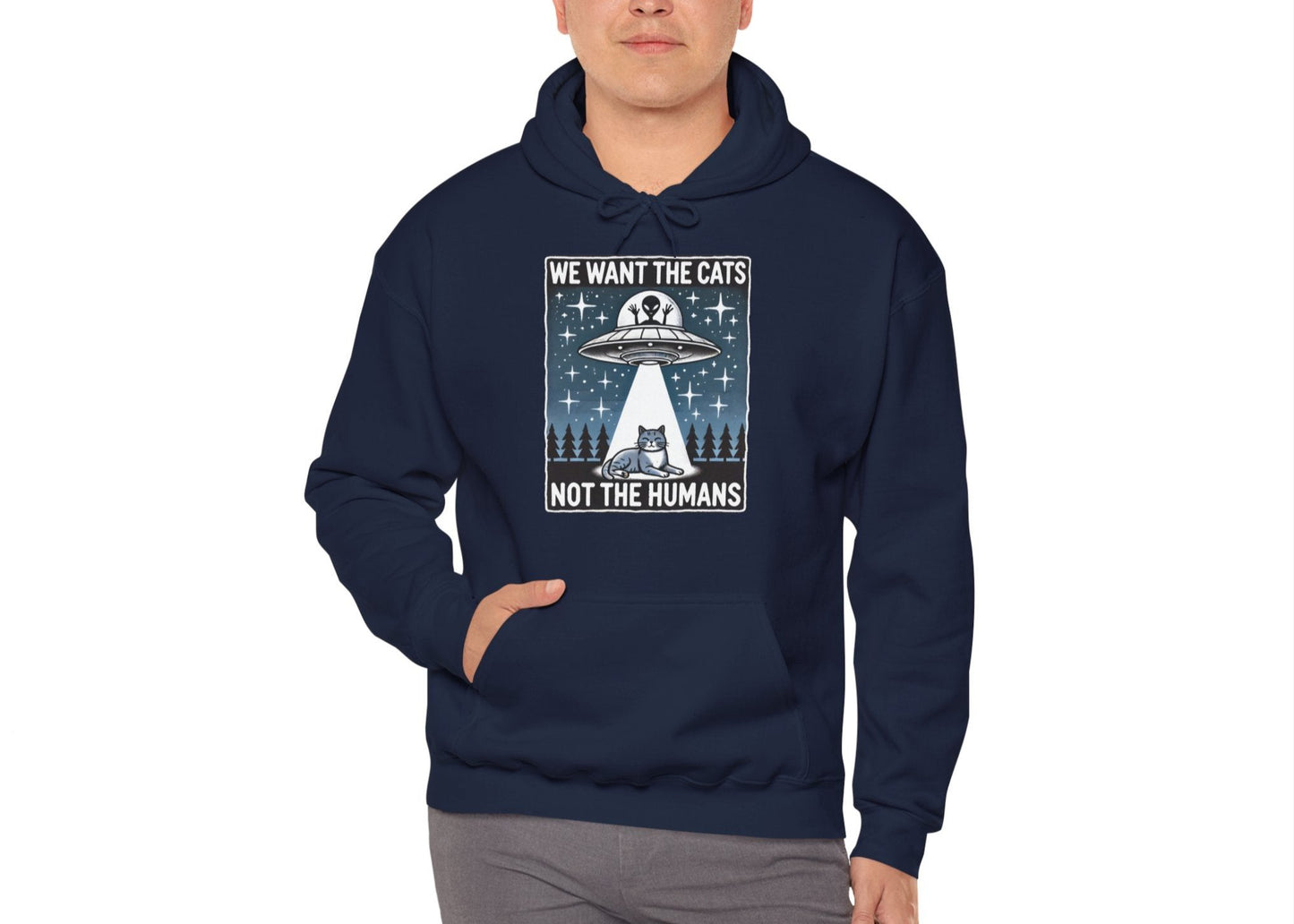 Model wearing a navy blue hoodie featuring the text "We Want the Cats, Not the Humans" with an illustration of a UFO beaming up cats. Part of the Vivid Divergence Sensory Friendly Unisex Hoodie Range.