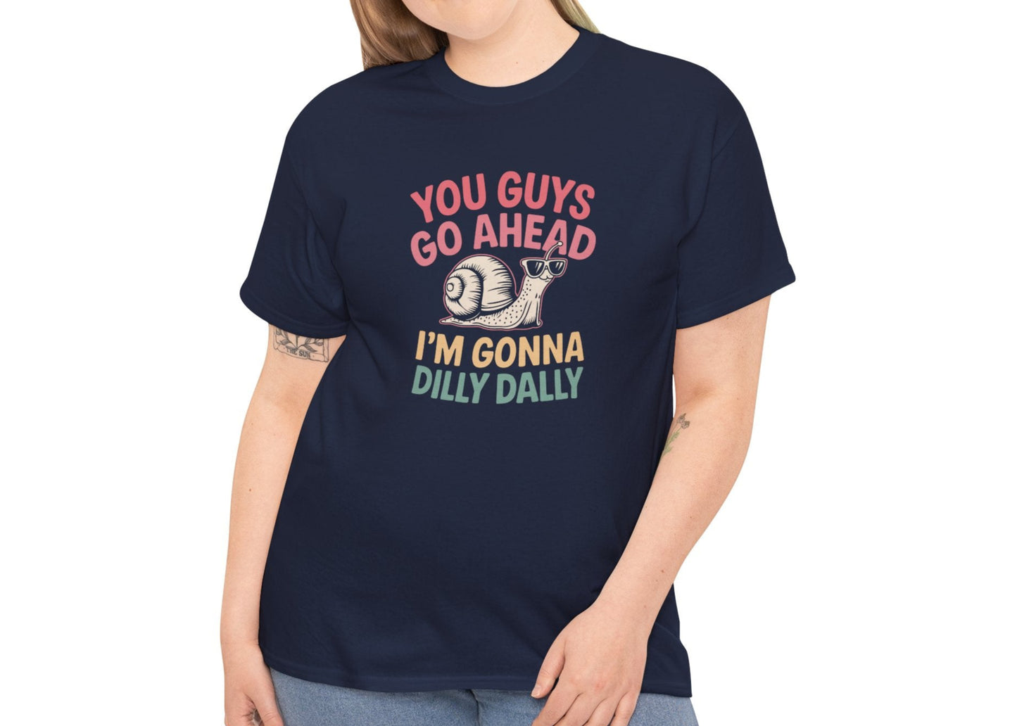 Model wearing a navy blue T-shirt featuring "You Guys Go Ahead, I'm Gonna Dilly Dally" text in a retro 90s-style font with a snail illustration. Part of the Vivid Divergence Sensory Friendly Unisex Tees Range.