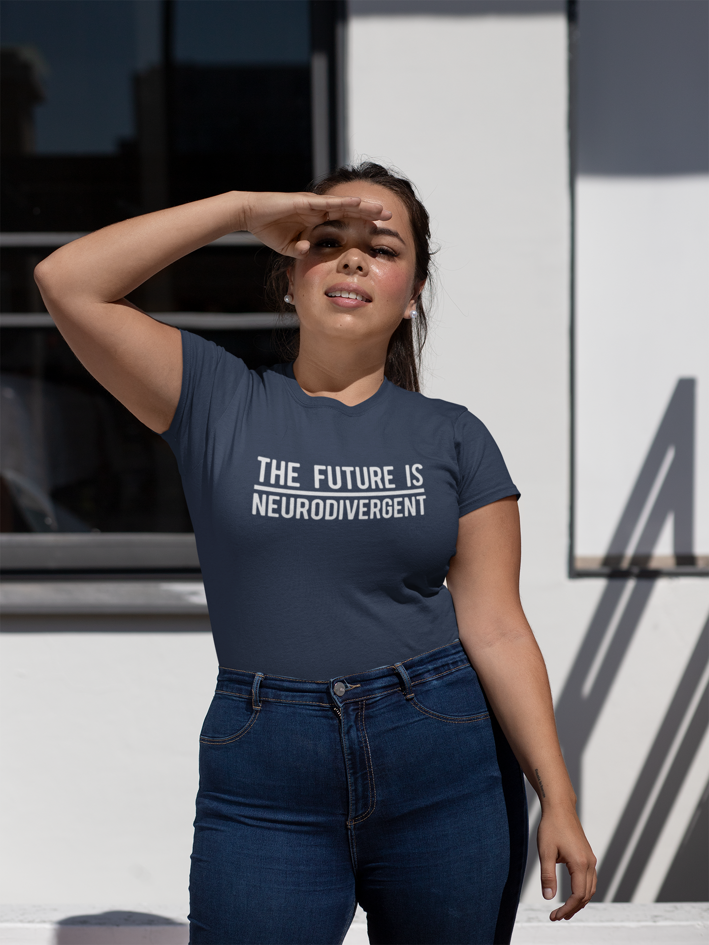 Model wearing a navy T-shirt with the text "The Future is Neurodivergent" in bold white letters, standing outdoors. Part of the Vivid Divergence Sensory Friendly Unisex Tees Range.