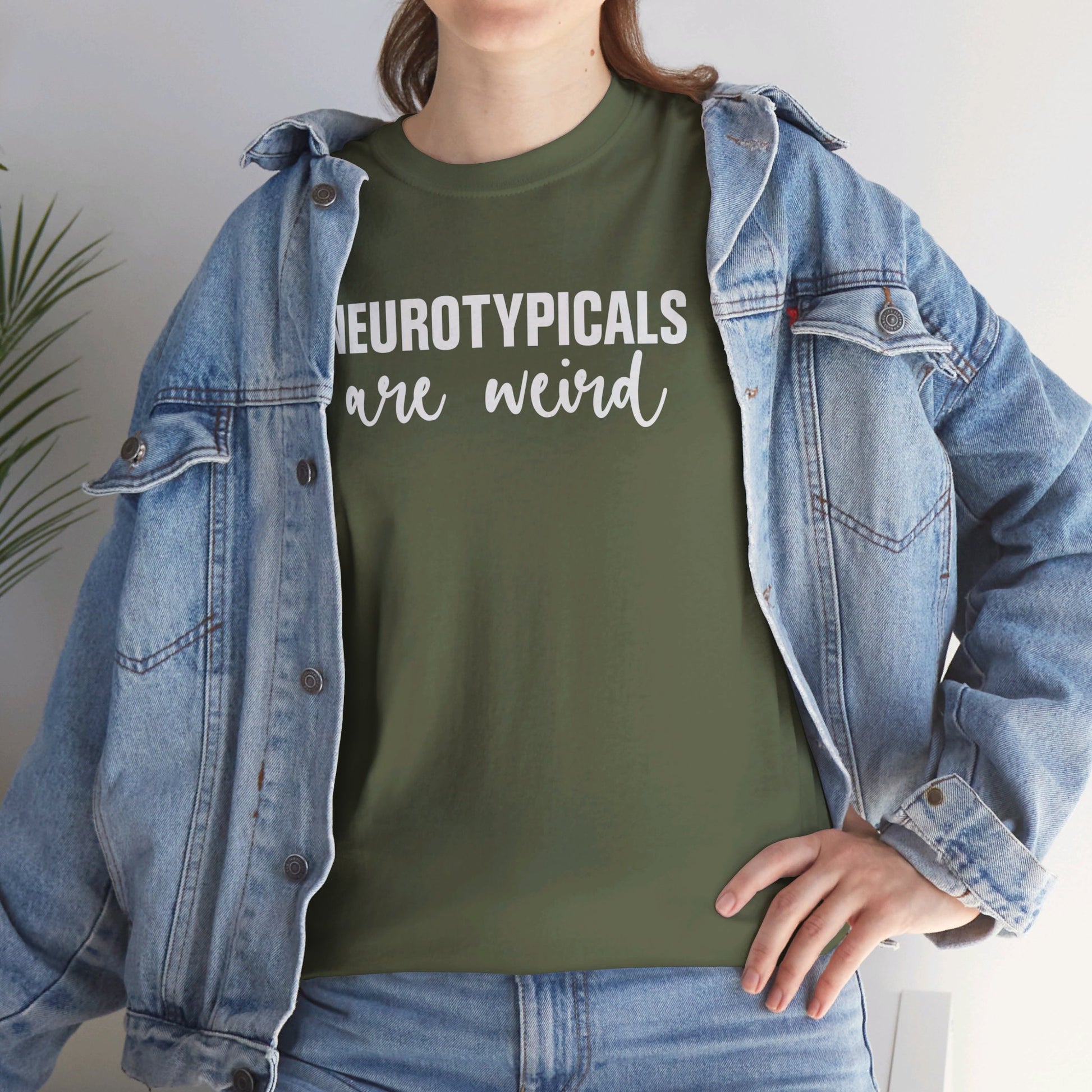 Model wearing an olive green T-shirt with "Neurotypicals Are Weird" in bold white text and a denim jacket. Part of the Vivid Divergence Sensory Friendly Unisex Tees Range.