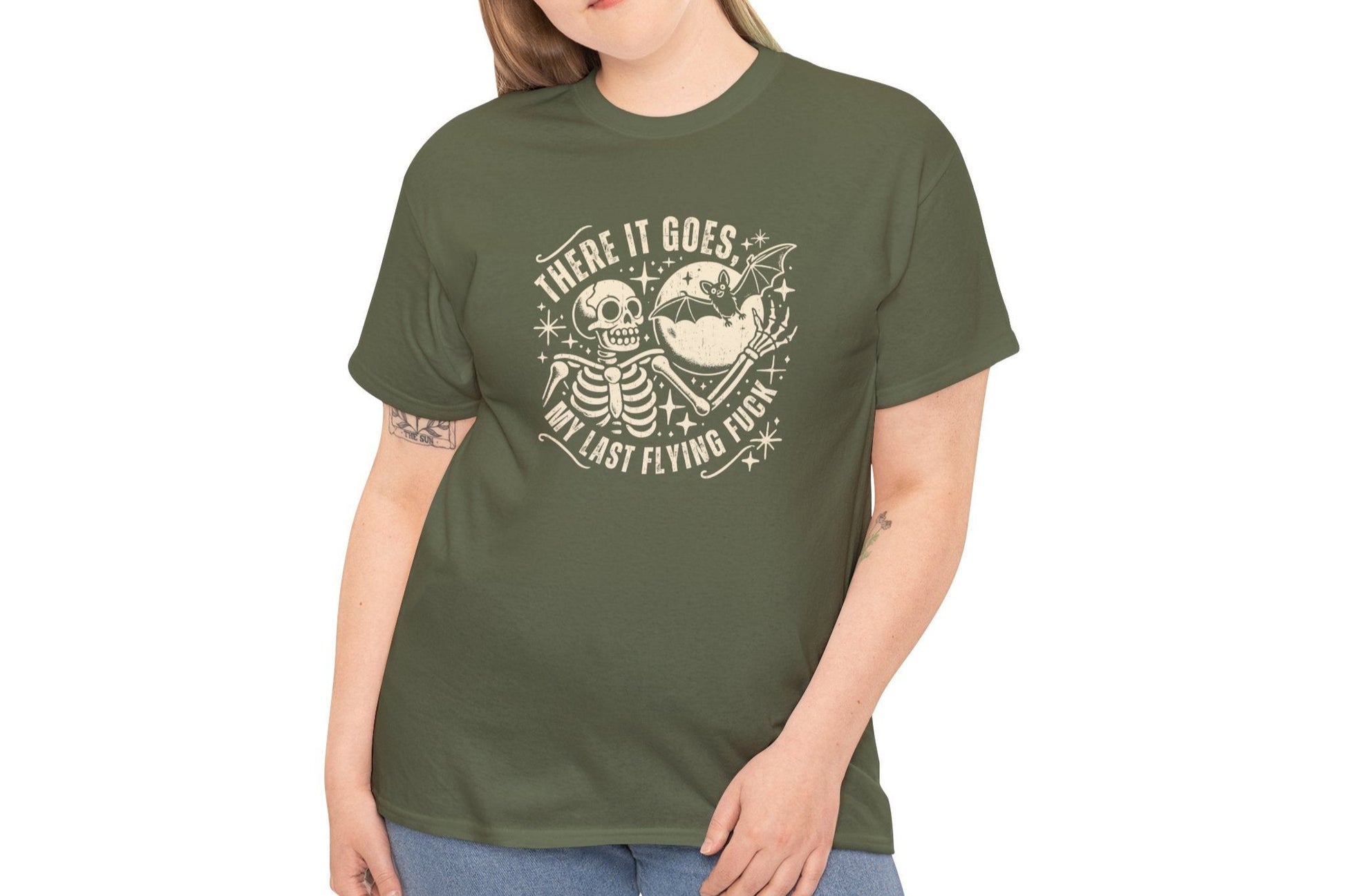 Model wearing an olive green T-shirt with the text "There It Goes, My Last Flying F*ck" and a graphic of a flying bird carrying a banner. Part of the Vivid Divergence Sensory Friendly Unisex Tees Range.
