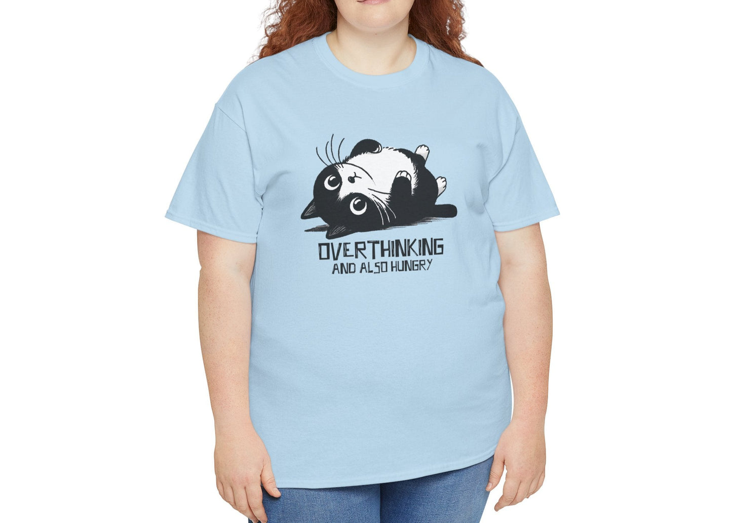 Modeled view of light blue T-shirt featuring black line art of a wide-eyed cat surrounded by scribbles, with the phrase "Overthinking and also hungry." A whole vibe. Part of the Vivid Divergence Memewear Collection!