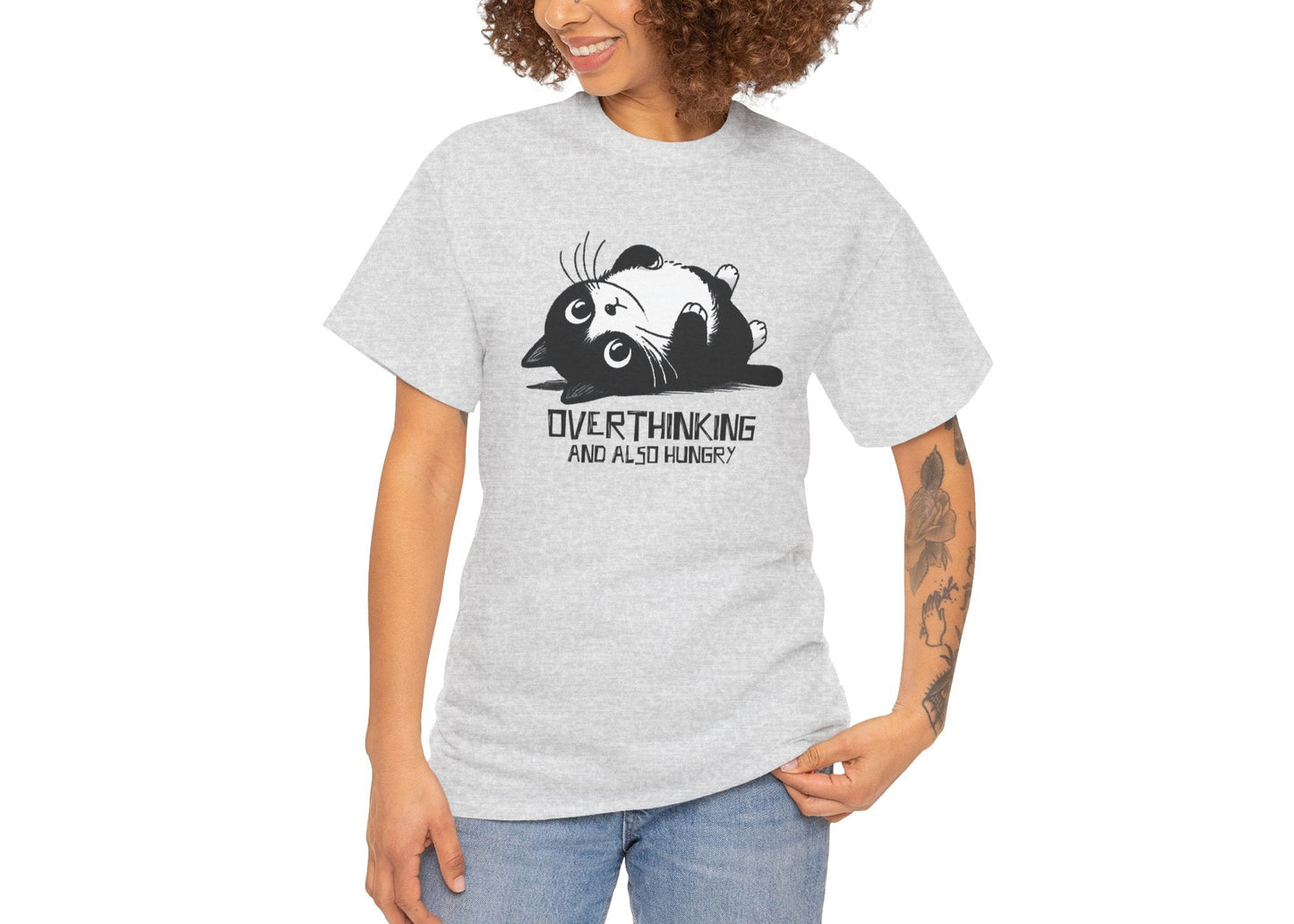 Modeled view of light grey T-shirt featuring black line art of a wide-eyed cat surrounded by scribbles, with the phrase "Overthinking and also hungry." A whole vibe. Part of the Vivid Divergence Memewear Collection!