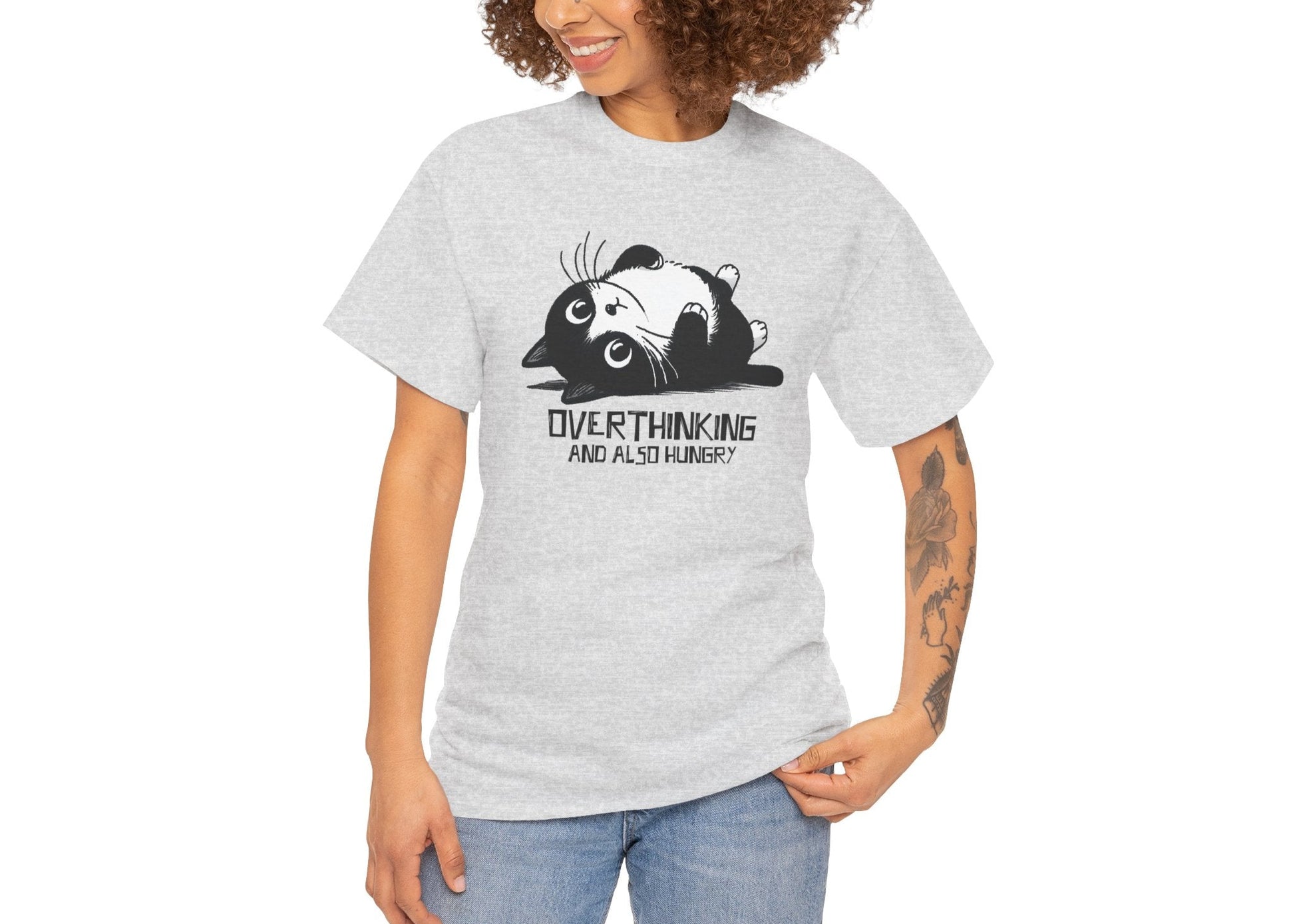 Modeled view of light grey T-shirt featuring black line art of a wide-eyed cat surrounded by scribbles, with the phrase "Overthinking and also hungry." A whole vibe. Part of the Vivid Divergence Memewear Collection!