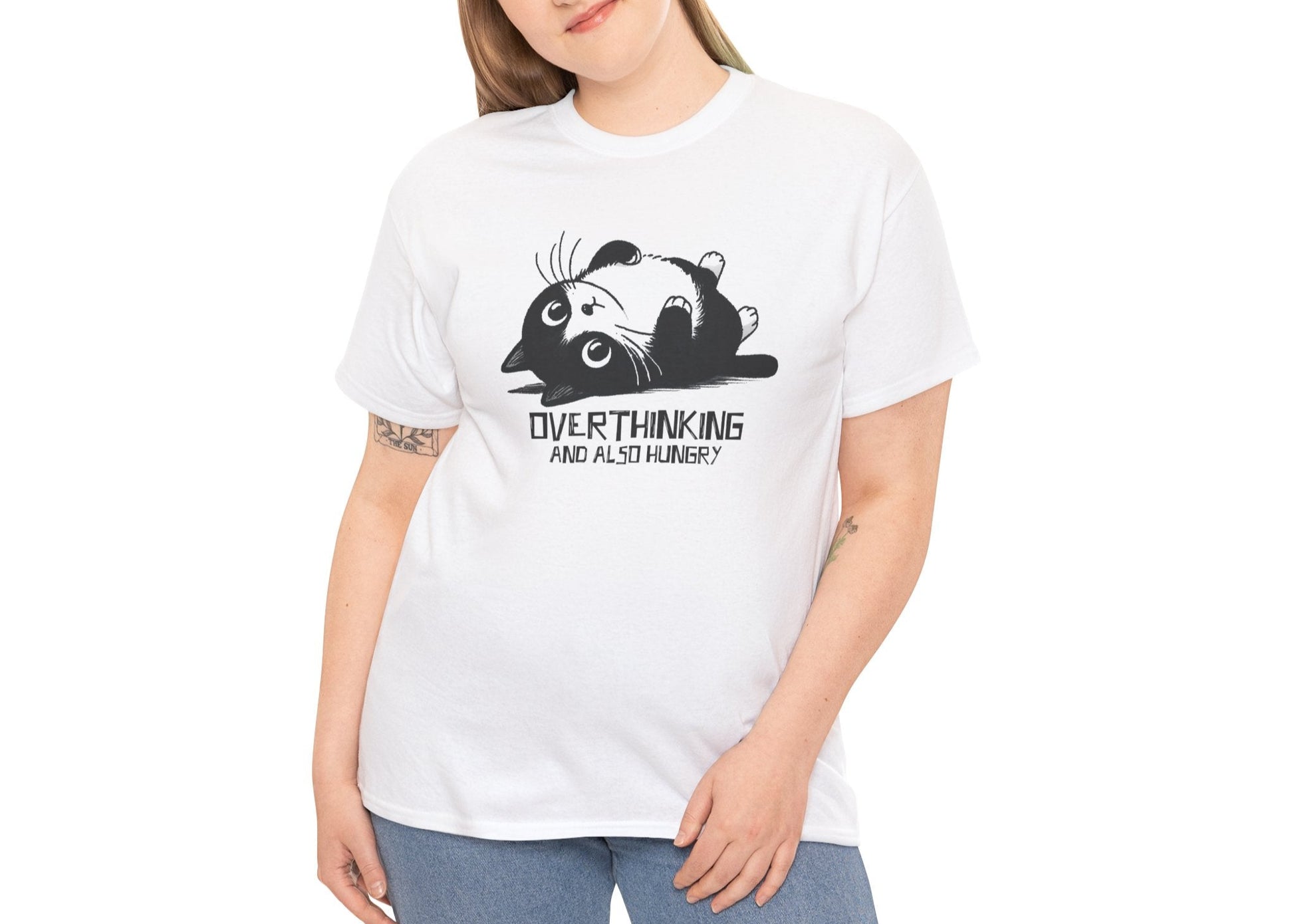 Modeled view of white T-shirt featuring black line art of a wide-eyed cat surrounded by scribbles, with the phrase "Overthinking and also hungry." A whole vibe. Part of the Vivid Divergence Memewear Collection!
