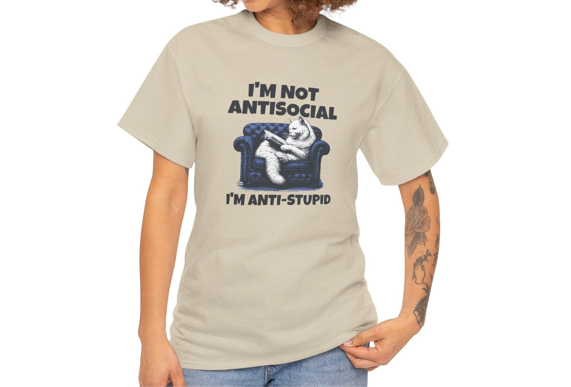 A person wearing a beige T-shirt with a graphic of a cat on a couch and the text "I'm Not Anti-Social, I'm Anti-Stupid." Part of the Vivid Divergence Sensory Friendly Unisex Tees Range.