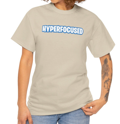A person wearing a beige T-shirt with the text "Hyperfocused" in a Fortnite-style design. Part of the Vivid Divergence Sensory Friendly Unisex Tees Range.