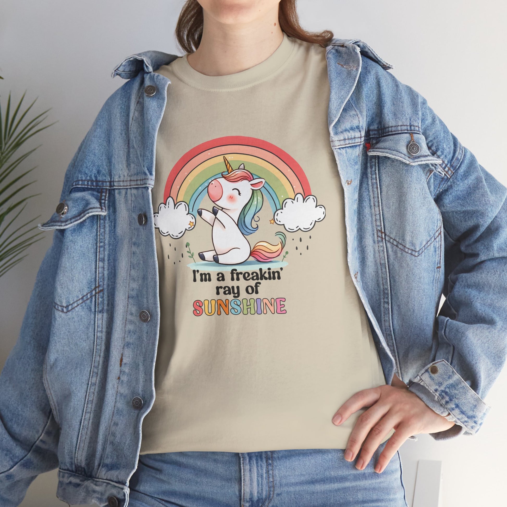 A person wearing a beige T-shirt with a rainbow and unicorn graphic and the text "I'm A Freakin Ray Of Sunshine." Part of the Vivid Divergence Sensory Friendly Unisex Tees Range.