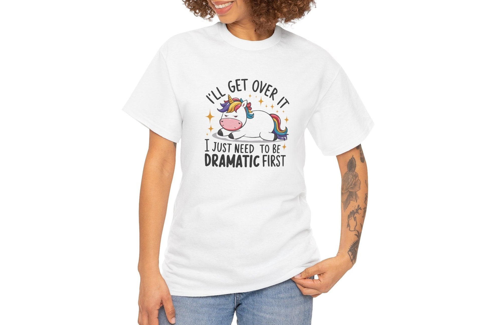 A person wearing a white T-shirt with a unicorn and cow graphic and the text "I'll Get Over It, I Just Need To Be Dramatic First." Part of the Vivid Divergence Sensory Friendly Unisex Tees Range.