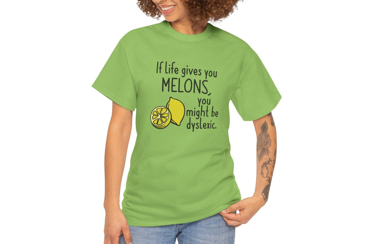 A person wearing a green T-shirt with a lemon and melon graphic and the text "If life gives you melons, you might be dyslexic." Part of the Vivid Divergence Sensory Friendly Unisex Tees Range.