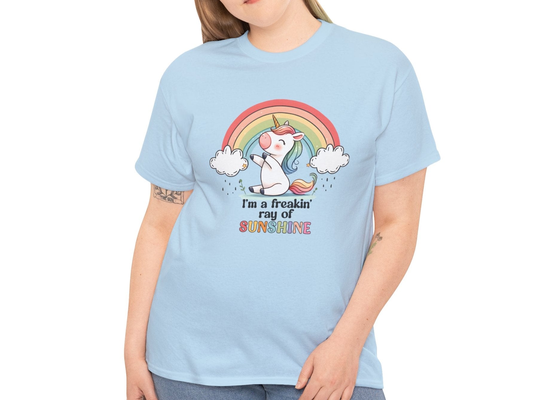 A person wearing a light blue T-shirt with a rainbow and unicorn graphic and the text "I'm A Freakin Ray Of Sunshine." Part of the Vivid Divergence Sensory Friendly Unisex Tees Range.