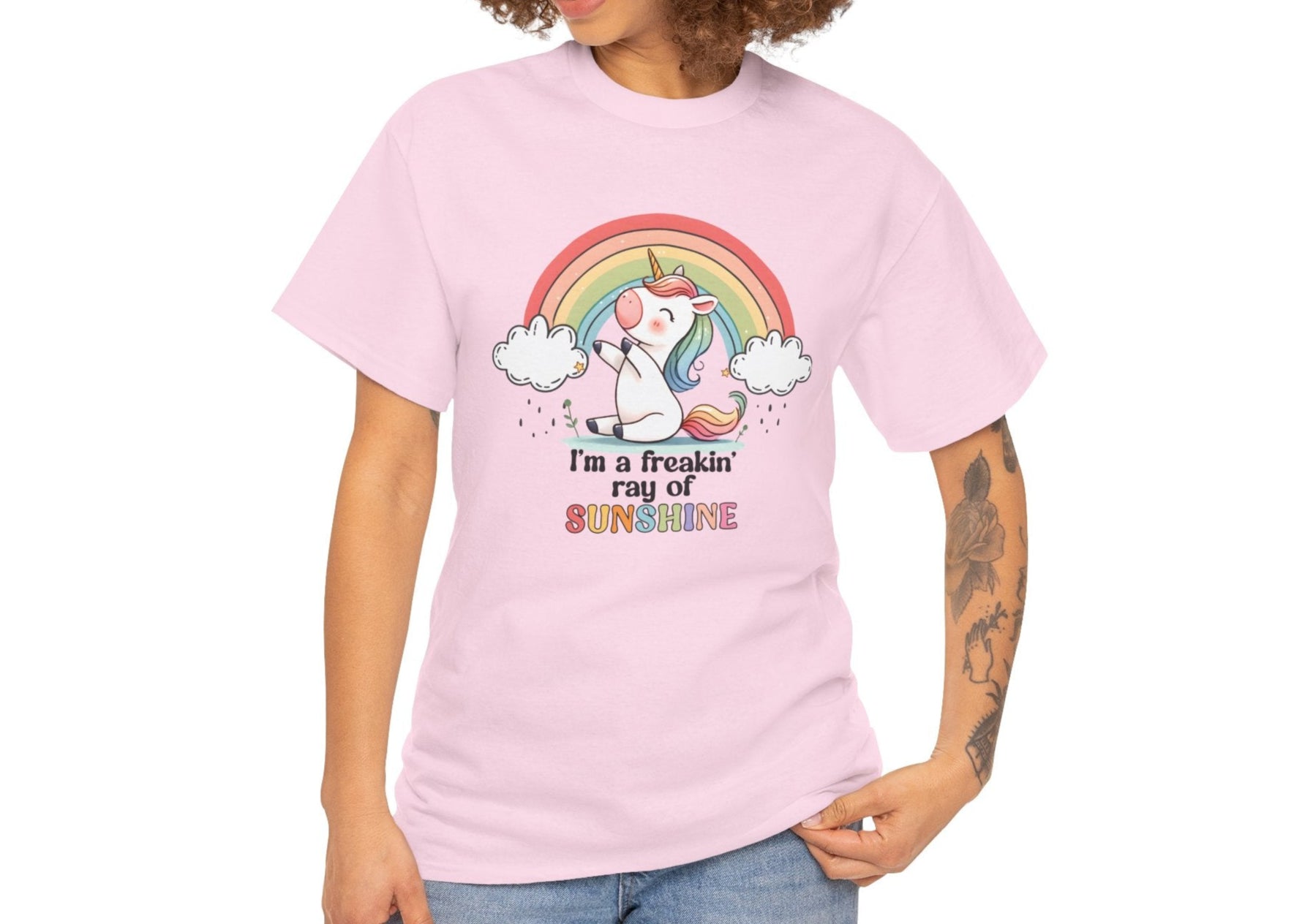 A person wearing a light pink T-shirt with a rainbow and unicorn graphic and the text "I'm A Freakin Ray Of Sunshine." Part of the Vivid Divergence Sensory Friendly Unisex Tees Range.