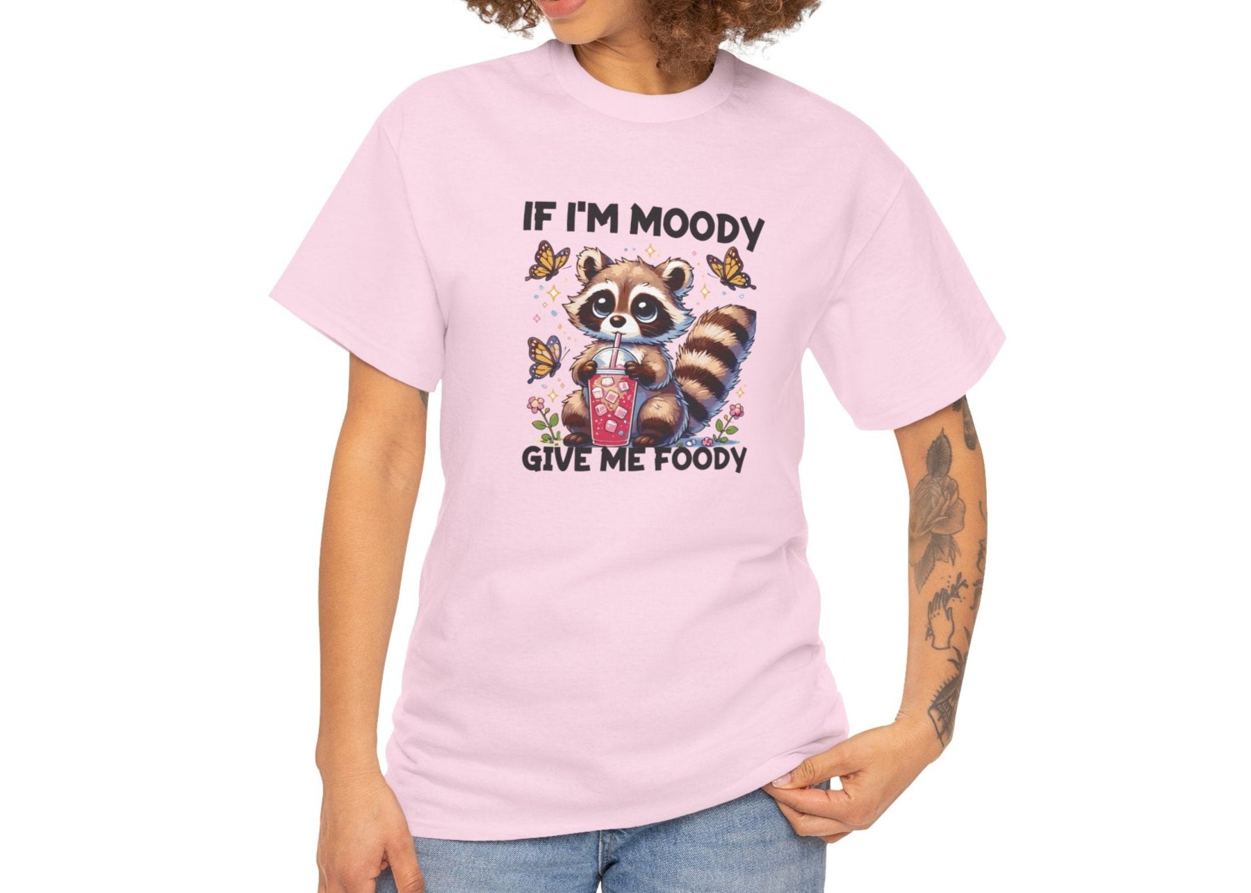 A person wearing a pink T-shirt with a raccoon graphic and the text "If I'm Moody, Give Me Foody." Part of the Vivid Divergence Sensory Friendly Unisex Tees Range.