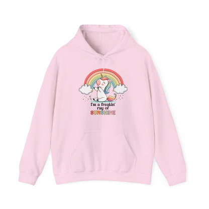 Front view of a pink hoodie featuring a grumpy-looking unicorn with wings under a rainbow, with the text "I'm a Freakin' Ray of Sunshine." Part of the Vivid Divergence Sensory Friendly Unisex Hoodie Range.