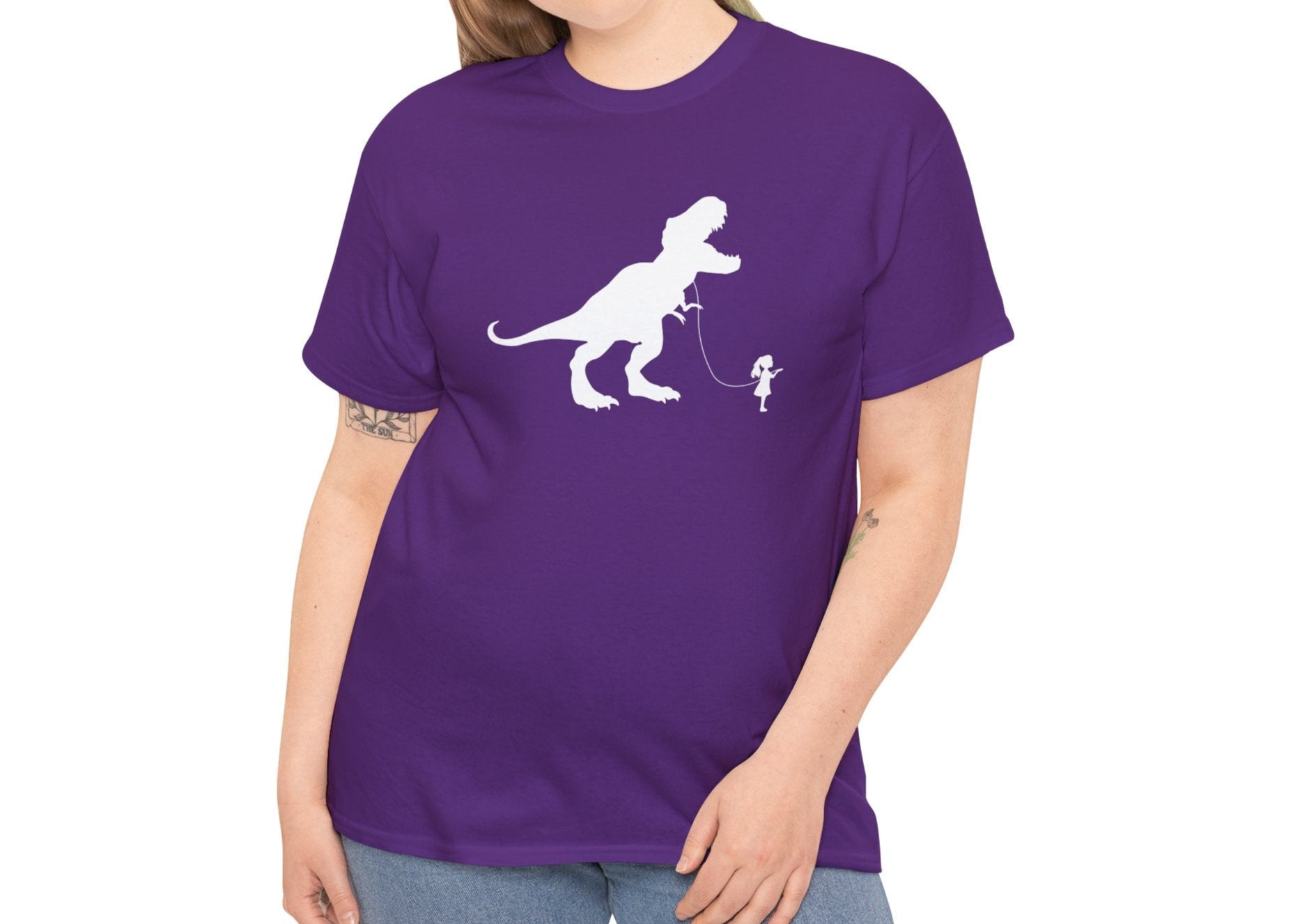 Model wearing a purple T-shirt featuring a white silhouette of a girl walking a T-Rex on a leash. Part of the Vivid Divergence Sensory Friendly Unisex Tees Range.