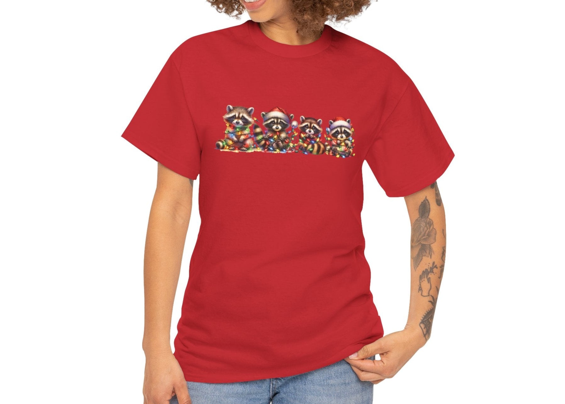 Model wearing a red T-shirt featuring a festive illustration of raccoons in Christmas attire causing holiday chaos, styled casually. Part of the Vivid Divergence Sensory Friendly Unisex Tees Range.