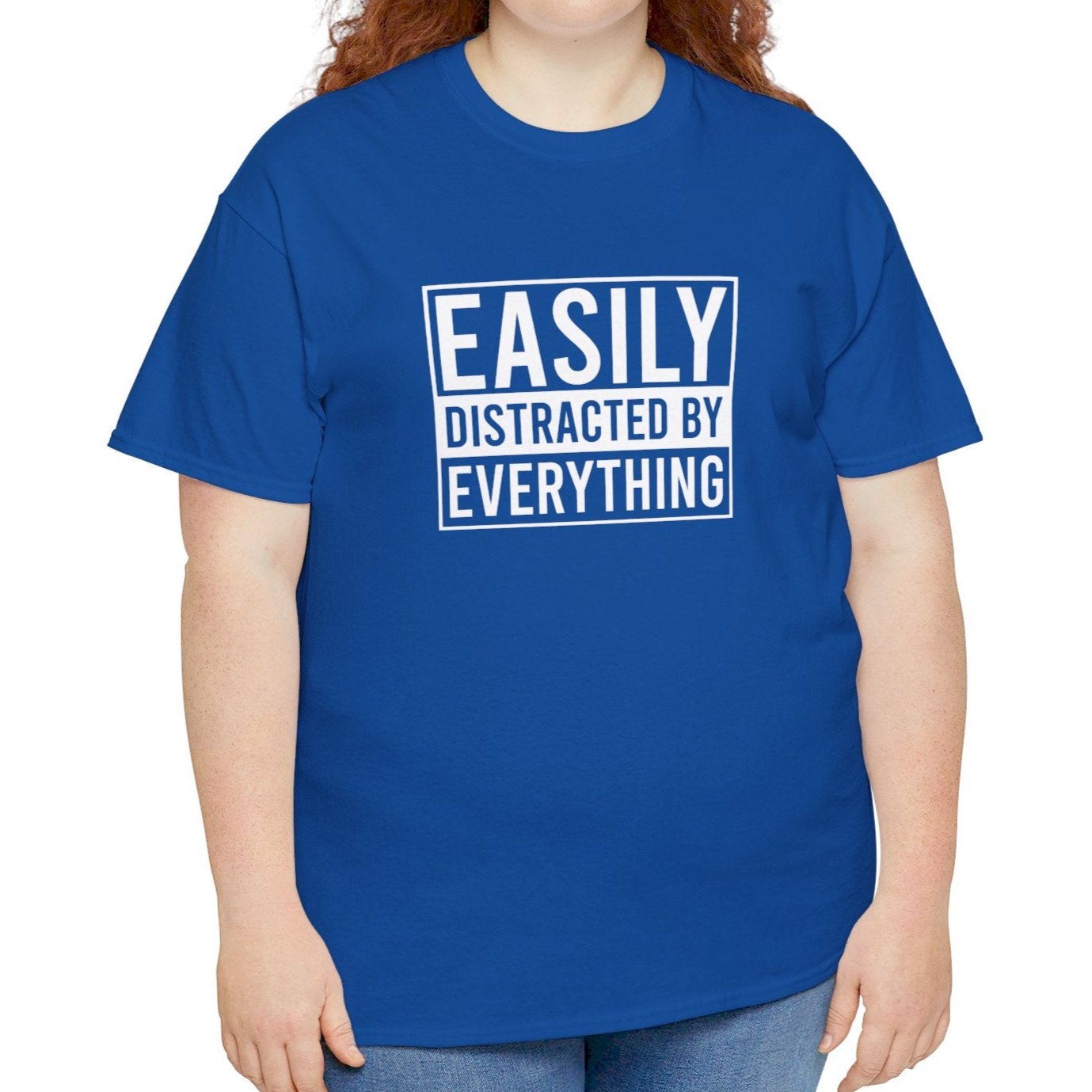 A person wearing a royal blue T-shirt with "Easily Distracted by Everything" text, shown from the front in a relaxed stance. Part of the Vivid Divergence Sensory Friendly Unisex Tees Range.