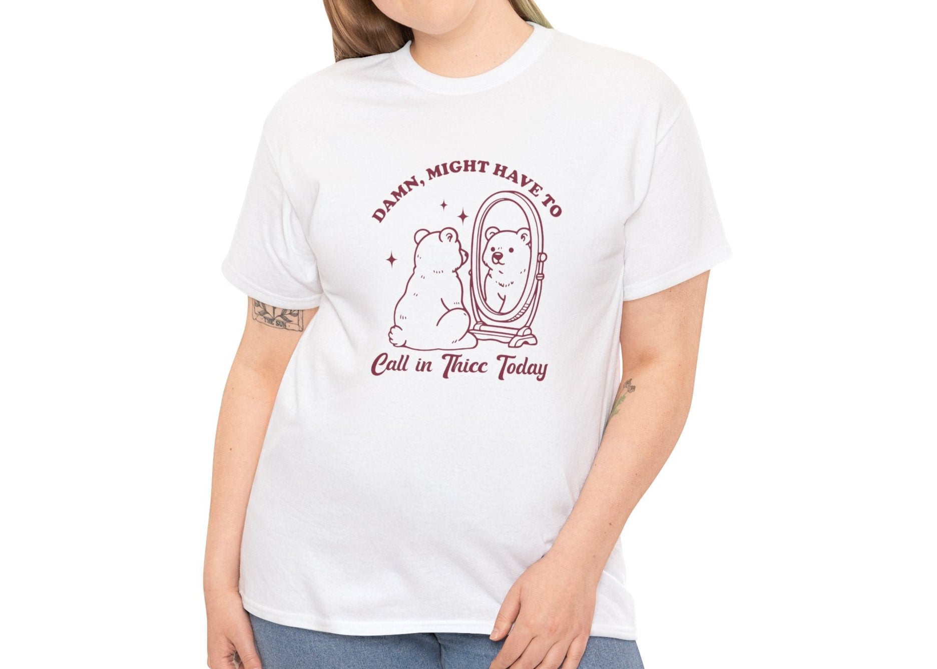Woman wearing a white T-shirt with a sitting bear in front of a mirror and "Damn, Might Have to Calling in Thicc Today" text in red. Part of the Vivid Divergence Sensory Friendly Unisex Tees Range.