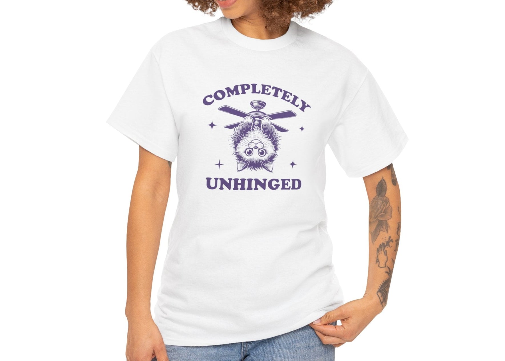 Front view of a white T-shirt featuring "Completely Unhinged" text with a cat hanging upside down from a ceiling fan in navy blue-tone design. Part of the Vivid Divergence Sensory Friendly Unisex Tees Range.