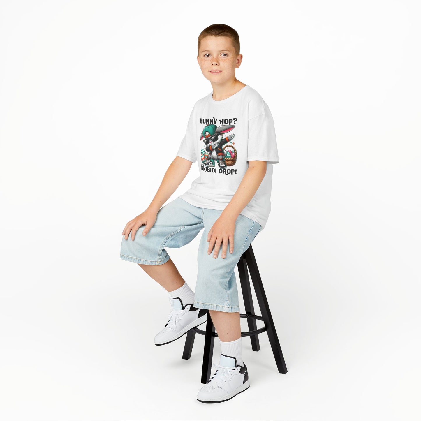 White skibidi drop bunny T-shirt worn by a boy sitting on a stool. A fun, bold shirt radiating skibidi sigma rizz energy for Easter. Hop into the season in style and shop Easter shirts online today!
