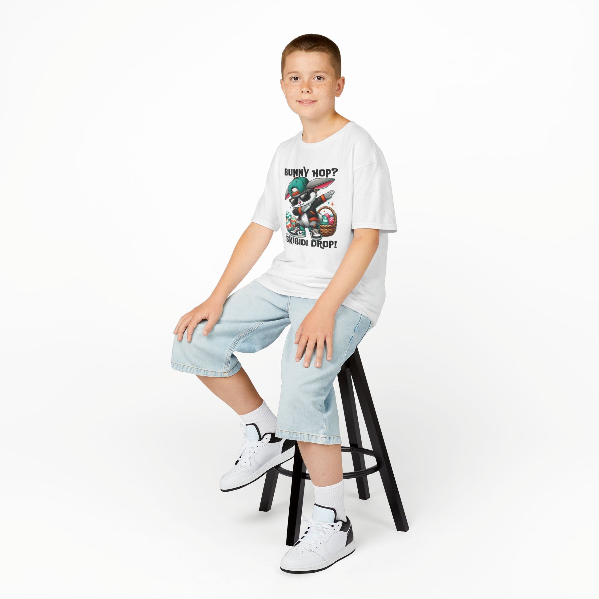 White skibidi drop bunny T-shirt worn by a boy sitting on a stool. A fun, bold shirt radiating skibidi sigma rizz energy for Easter. Hop into the season in style and shop Easter shirts online today!
