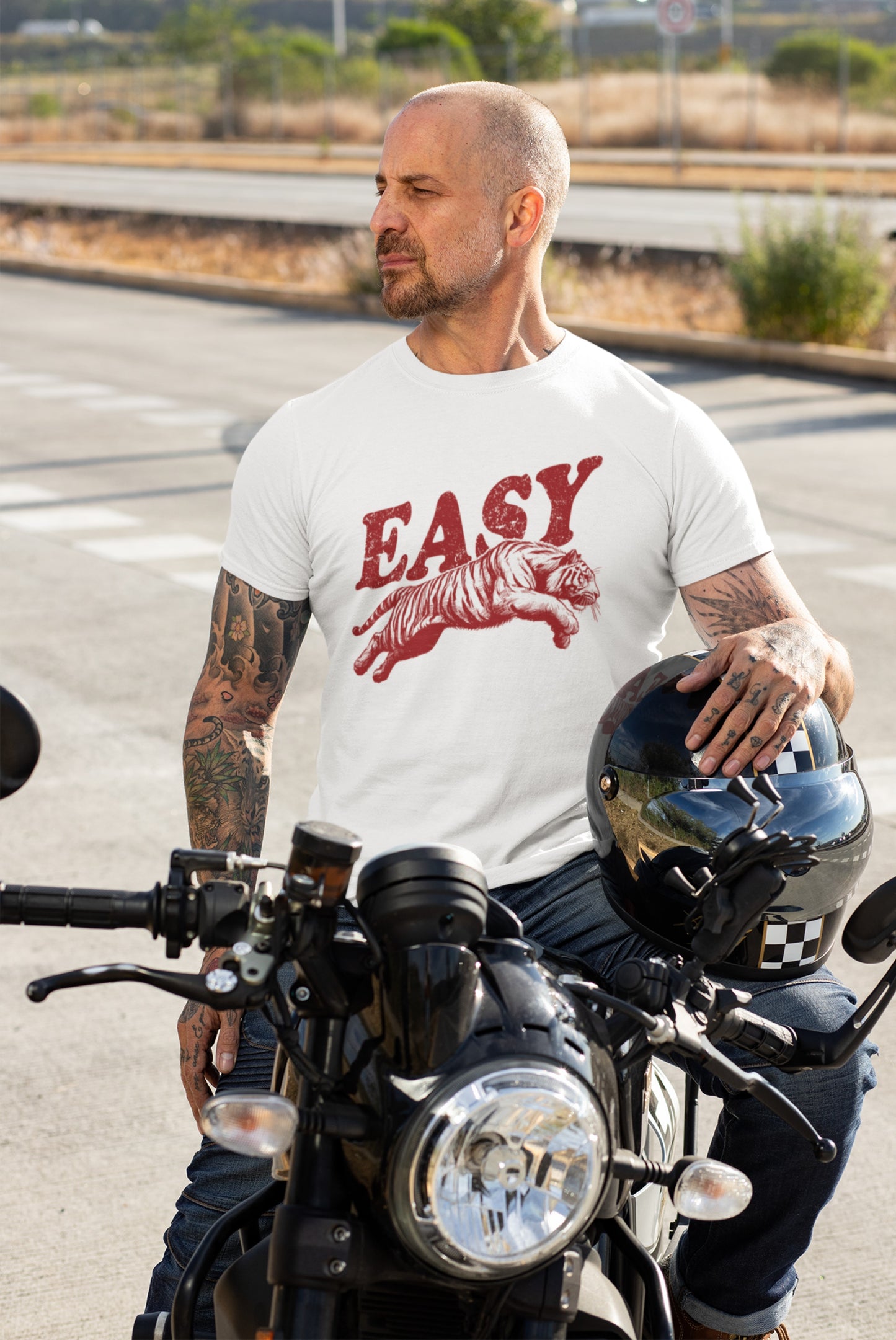 Man wearing a white T-shirt with "EASY" text and tiger illustration in black, standing beside a motorcycle. Part of the Vivid Divergence Sensory Friendly Unisex Tees Range.