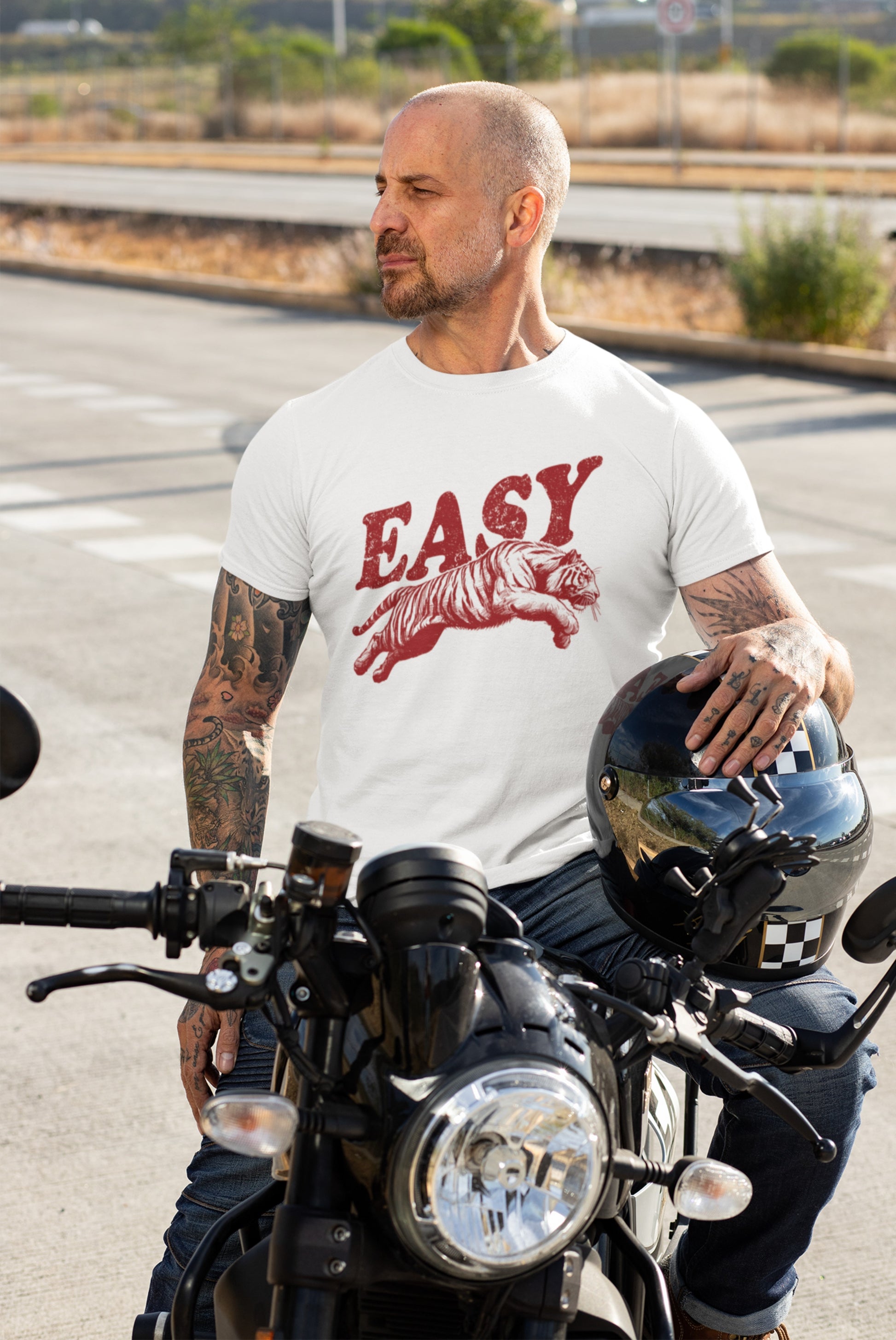 Man wearing a white T-shirt with "EASY" text and tiger illustration in black, standing beside a motorcycle. Part of the Vivid Divergence Sensory Friendly Unisex Tees Range.