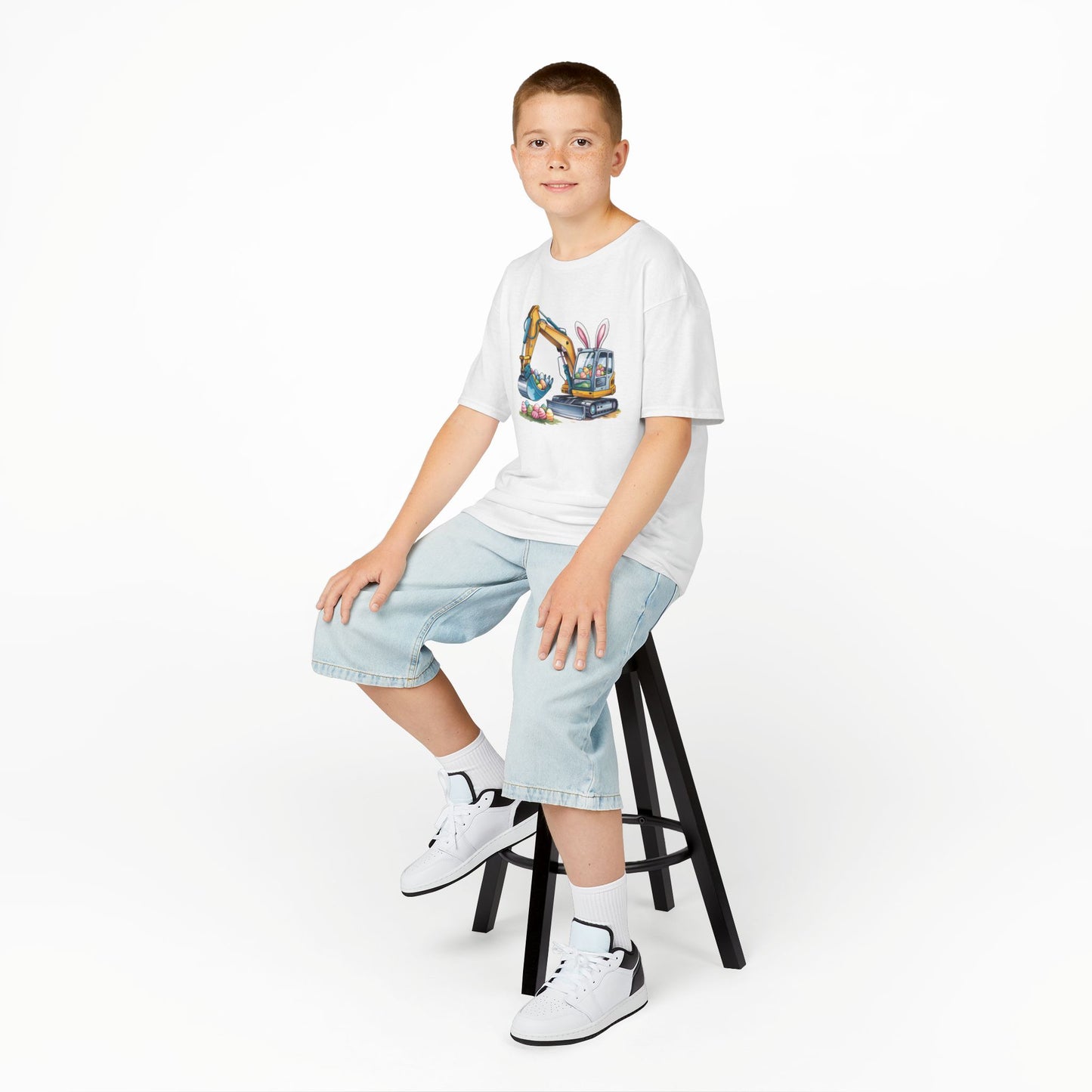 Child wearing a white Easter T-shirt featuring an excavator lifting festive eggs, perfect for young construction fans. Hop into the season in style and shop Easter shirts online today!