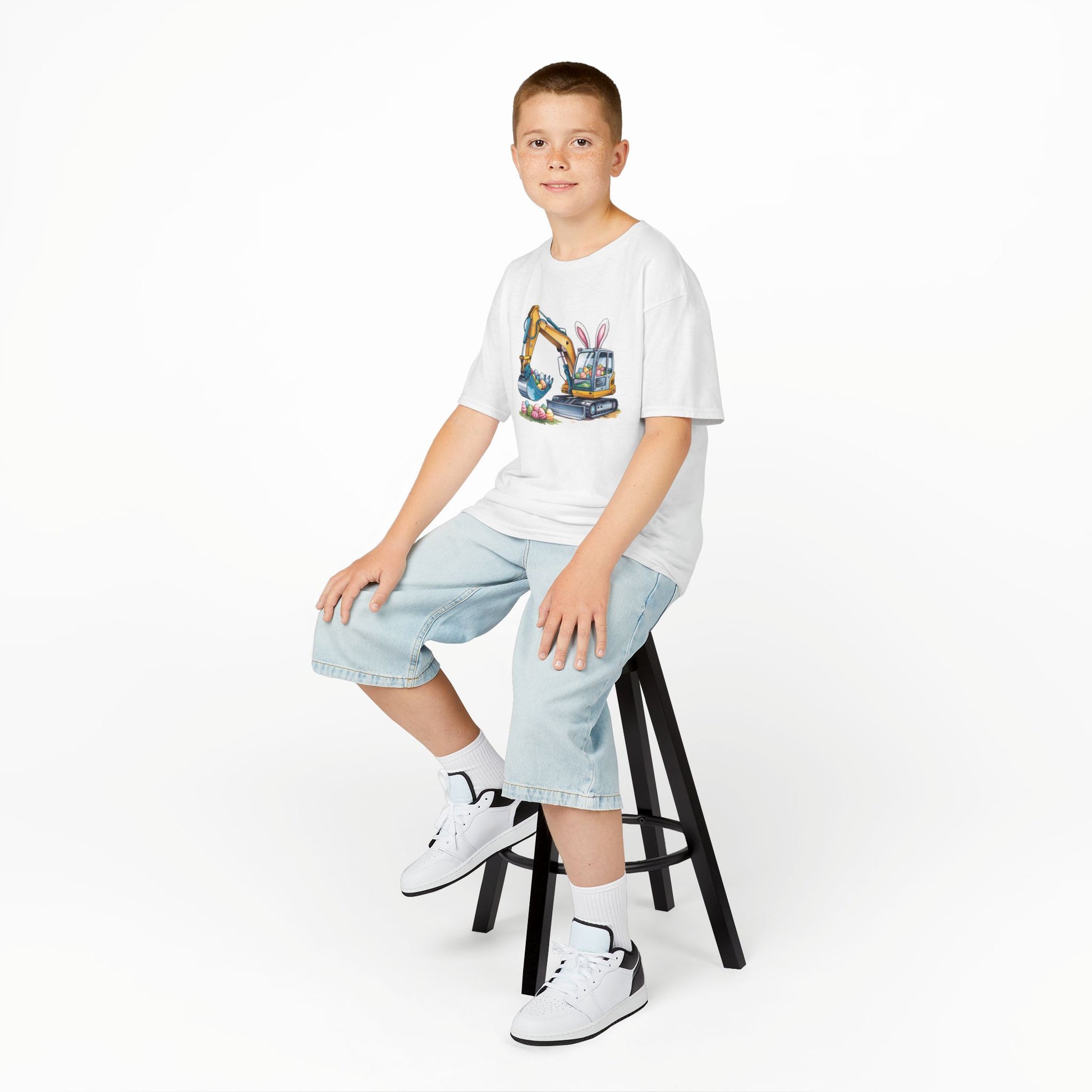 Child wearing a white Easter T-shirt featuring an excavator lifting festive eggs, perfect for young construction fans. Hop into the season in style and shop Easter shirts online today!