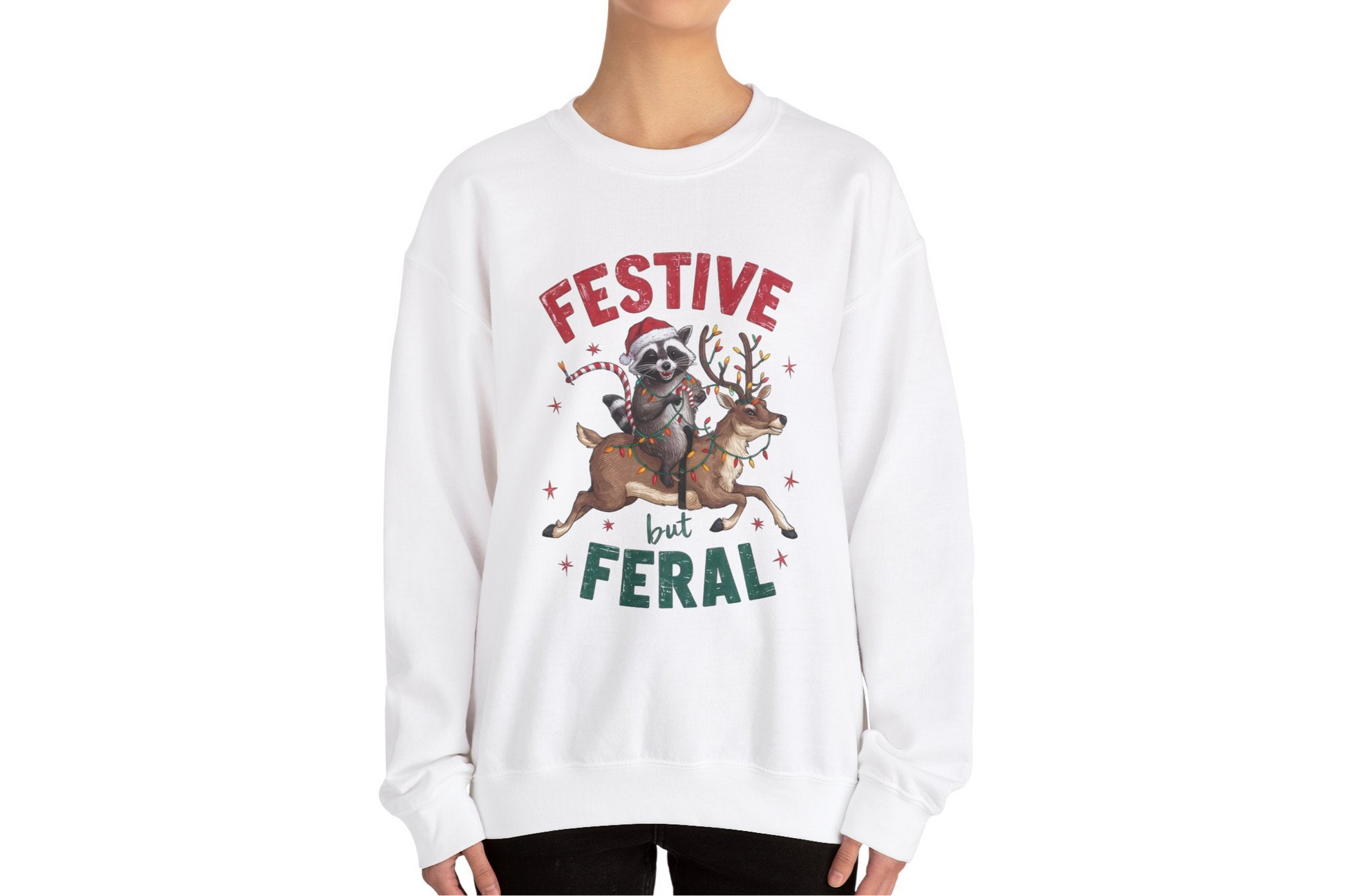 Model wearing a white sweatshirt featuring a festive raccoon holding Christmas lights and the text "Festive but Feral," styled in a casual holiday setting. Part of the Vivid Divergence Sensory Friendly Unisex Sweater Jumper Range.