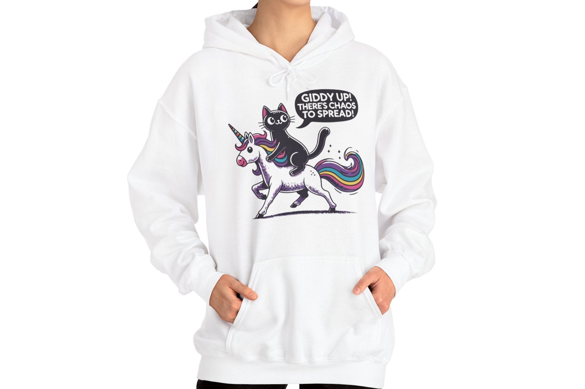 Model sitting while wearing a white hoodie featuring the text "Giddy Up, There’s Chaos to Spread" and a cartoon illustration of a cat riding a unicorn. Part of the Vivid Divergence Sensory Friendly Unisex Hoodie Range.