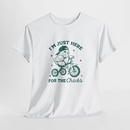 White T-shirt hanging, featuring a fun "I'm Just Here for the Chicks" design with a cute chick riding a bicycle, perfect for Easter celebrations. Hop into the season in style and shop Easter shirts online today!