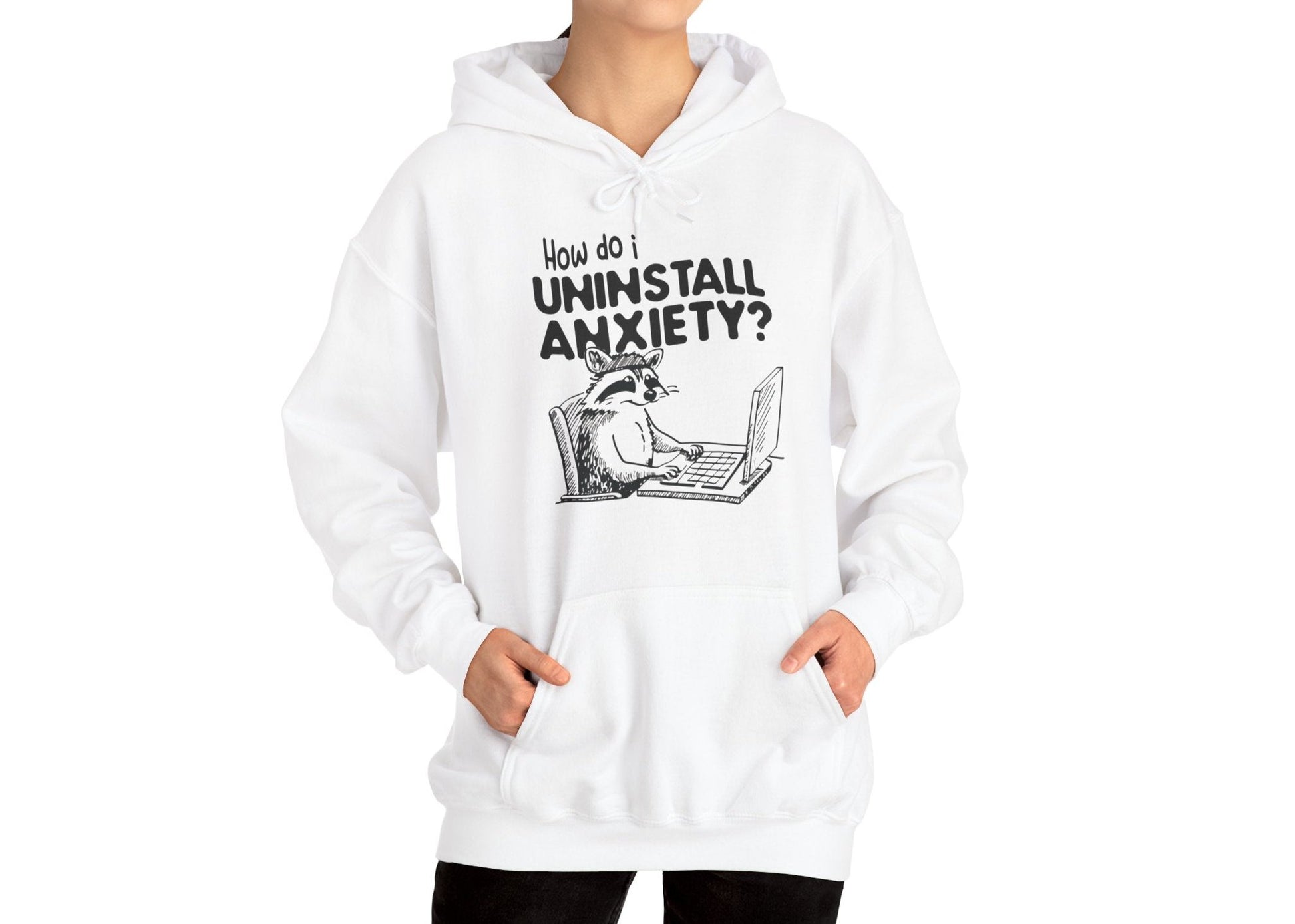 Model wearing a white hoodie featuring the text "How Do I Uninstall Anxiety?" and a cartoon illustration of a raccoon using a laptop. Part of the Vivid Divergence Sensory Friendly Unisex Hoodie Range.