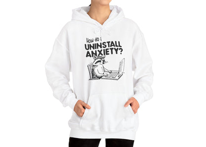 Model wearing a white hoodie featuring the text "How Do I Uninstall Anxiety?" and a cartoon illustration of a raccoon using a laptop. Part of the Vivid Divergence Sensory Friendly Unisex Hoodie Range.