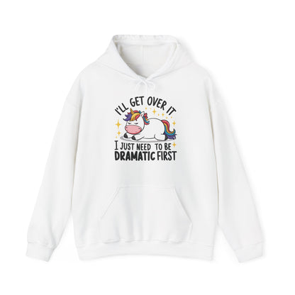 Front view of a white hoodie featuring a cartoon unicorn lying dramatically on a couch with the text "I'll Get Over It, I Just Need To Be Dramatic First." Part of the Vivid Divergence Sensory Friendly Unisex Hoodie Range.