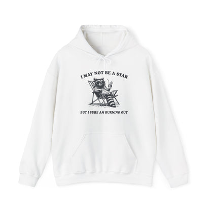 Front view of a white hoodie featuring a raccoon sitting in a trash can with the text "I May Not Be A Star, But I Sure Am Burning Out." Part of the Vivid Divergence Sensory Friendly Unisex Hoodie Range.