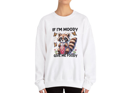 Model wearing a white sweater jumper with the text "If I'm Moody, Give Me Foody" and a cartoon raccoon illustration holding snacks. Part of the Vivid Divergence Sensory Friendly Unisex Sweater Jumper Range.