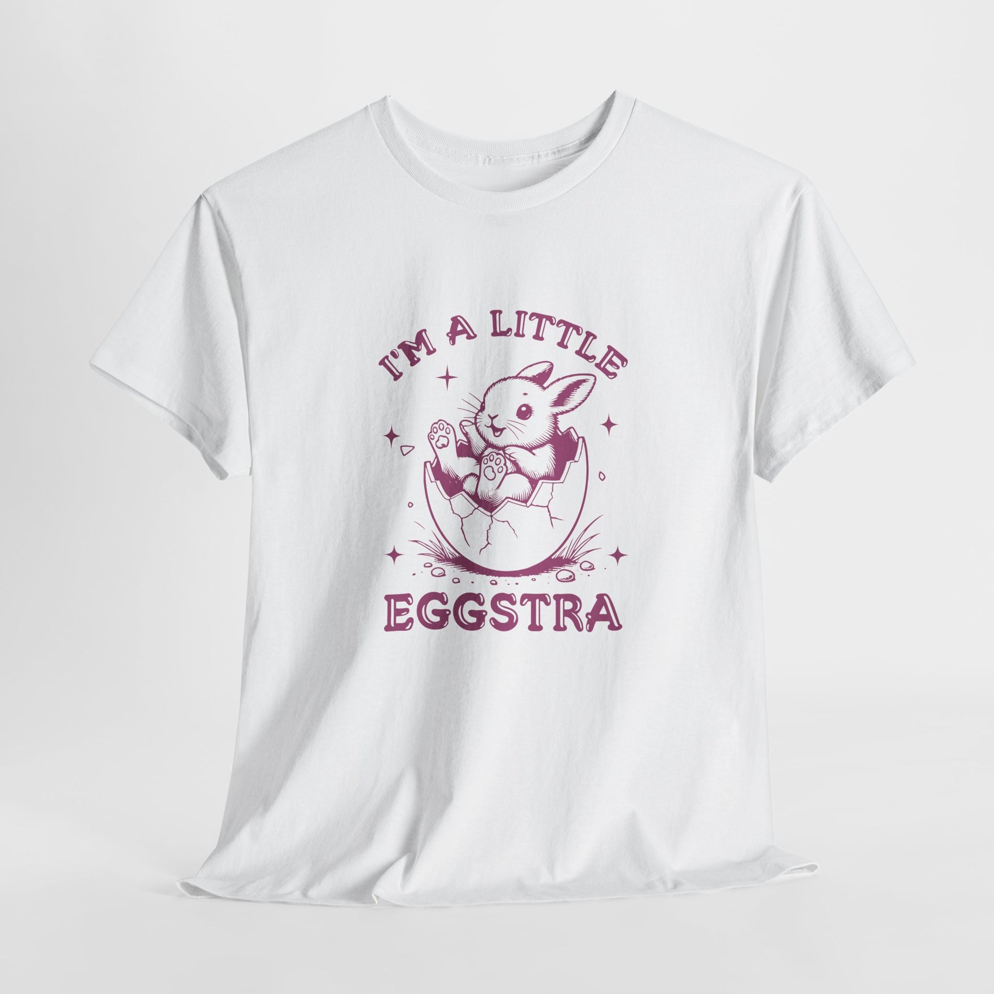 White Easter T-shirt hanging, showcasing a playful bunny and "I'm A Little Eggstra" text in a pink design, a stylish and festive choice. Hop into the season in style and shop Easter shirts online today!