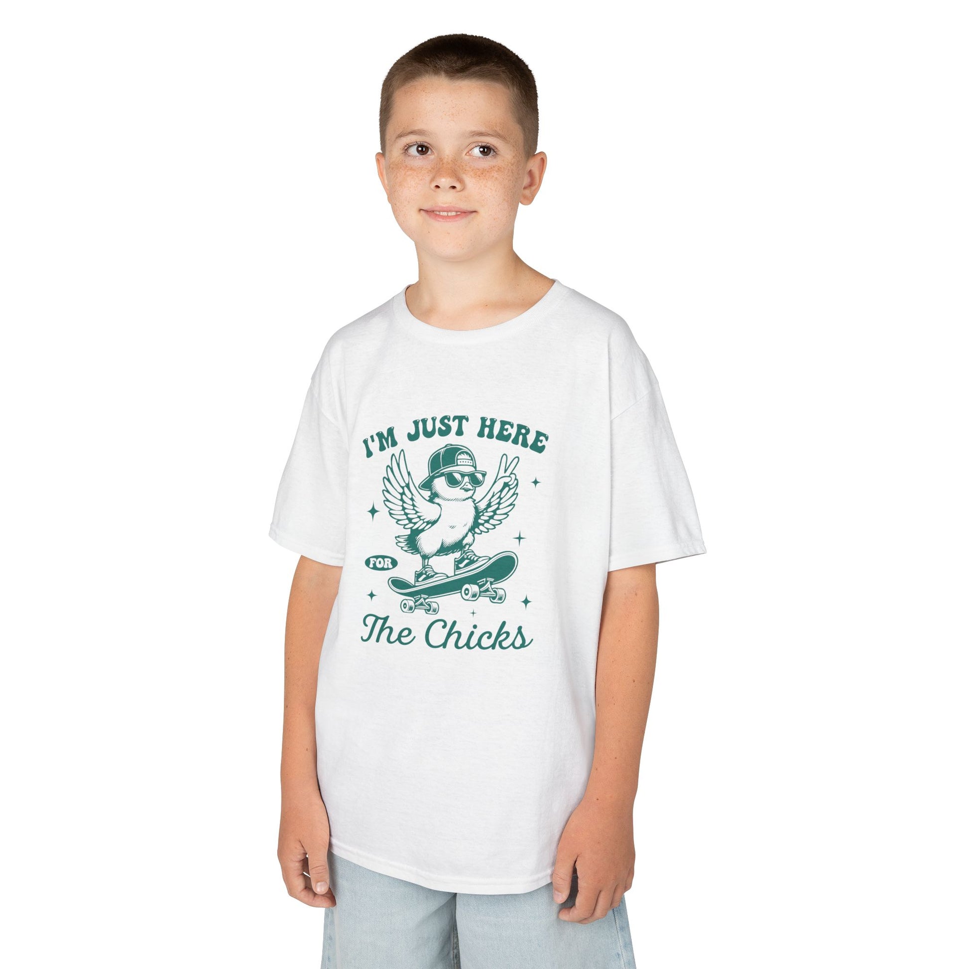 Child wearing a white Easter T-shirt with "I'm Just Here for the Chicks" text and a cute chick illustration, a humorous holiday look. Hop into the season in style and shop Easter shirts online today!