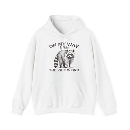 Front view of a white hoodie featuring the text "On My Way to Make the Vibe Weird" and a cartoon illustration of a raccoon holding a stick. Part of the Vivid Divergence Sensory Friendly Unisex Hoodie Range.