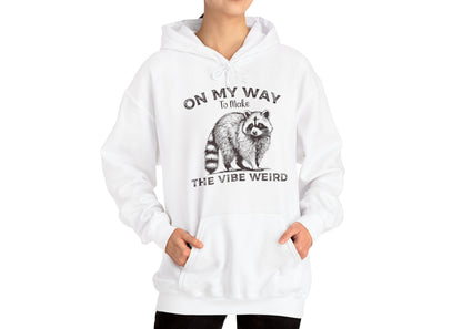 Model wearing a white hoodie featuring the text "On My Way to Make the Vibe Weird" and a cartoon illustration of a raccoon holding a stick. Part of the Vivid Divergence Sensory Friendly Unisex Hoodie Range.