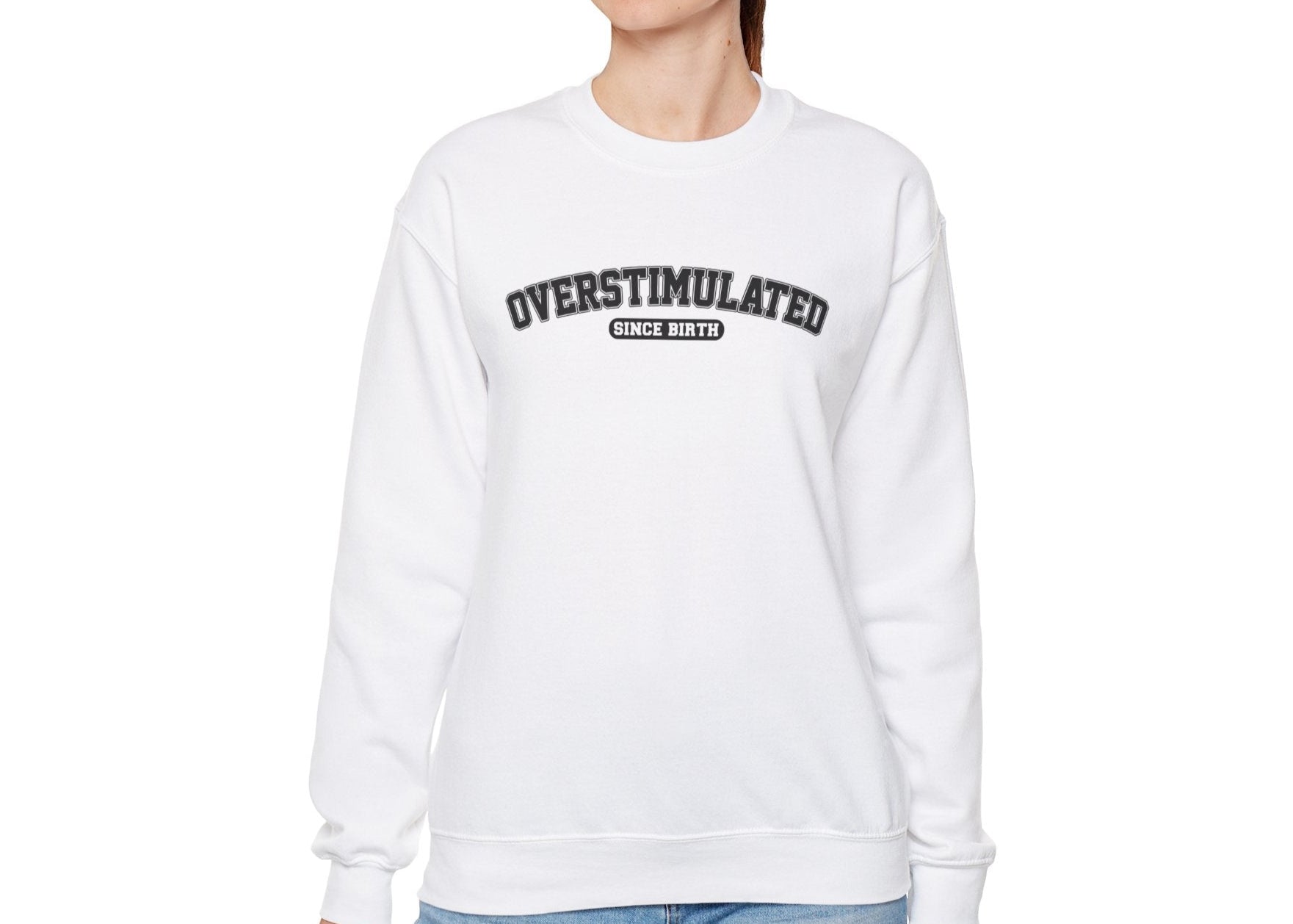 Model wearing a white sweater jumper with the text "Overstimulated Since Birth" in bold black lettering. Part of the Vivid Divergence Sensory Friendly Unisex Sweater Jumper Range.