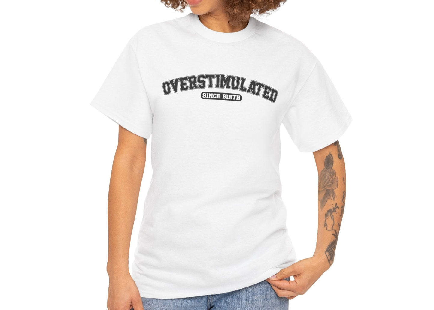 Model wearing a white T-shirt with "Overstimulated Since Birth" in bold black text. Part of the Vivid Divergence Sensory Friendly Unisex Tees Range.