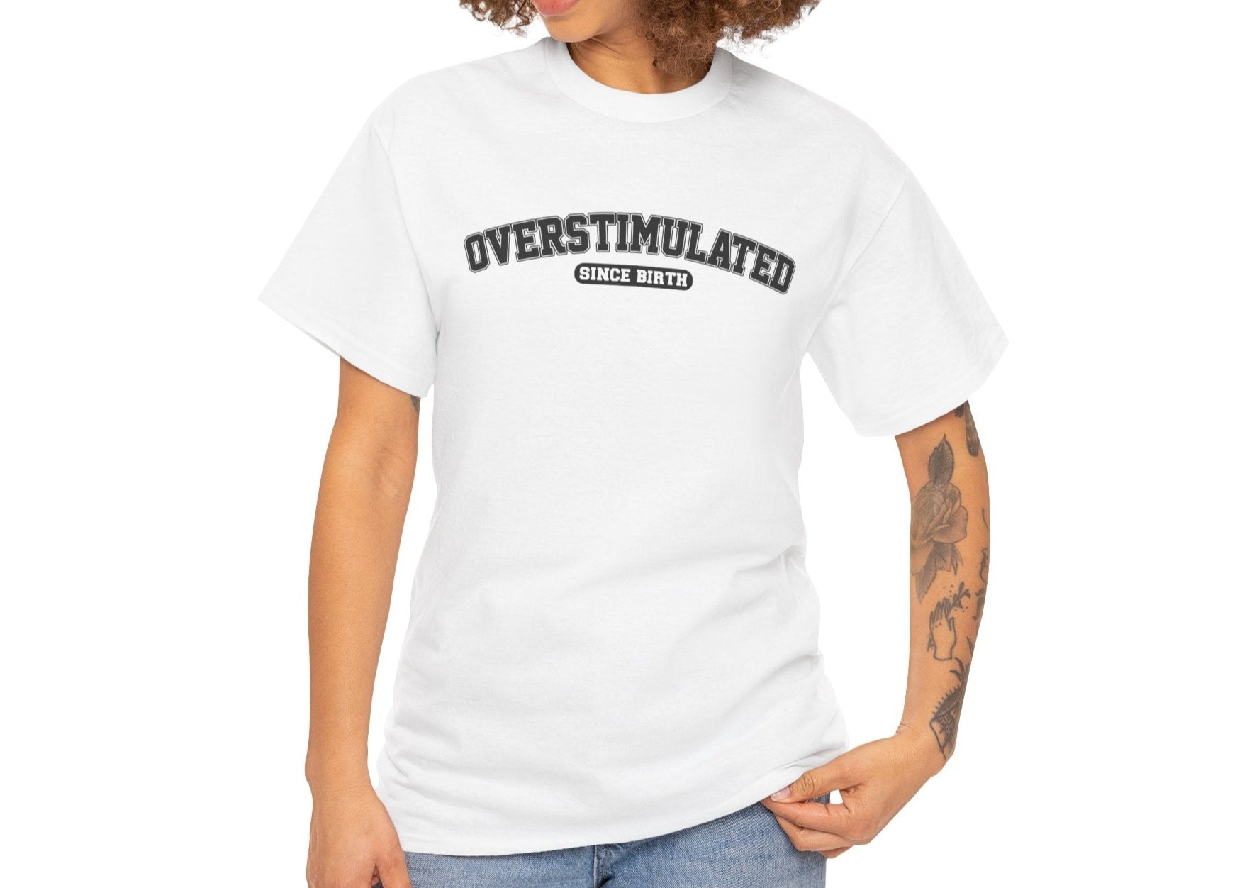 Model wearing a white T-shirt with "Overstimulated Since Birth" in bold black text. Part of the Vivid Divergence Sensory Friendly Unisex Tees Range.